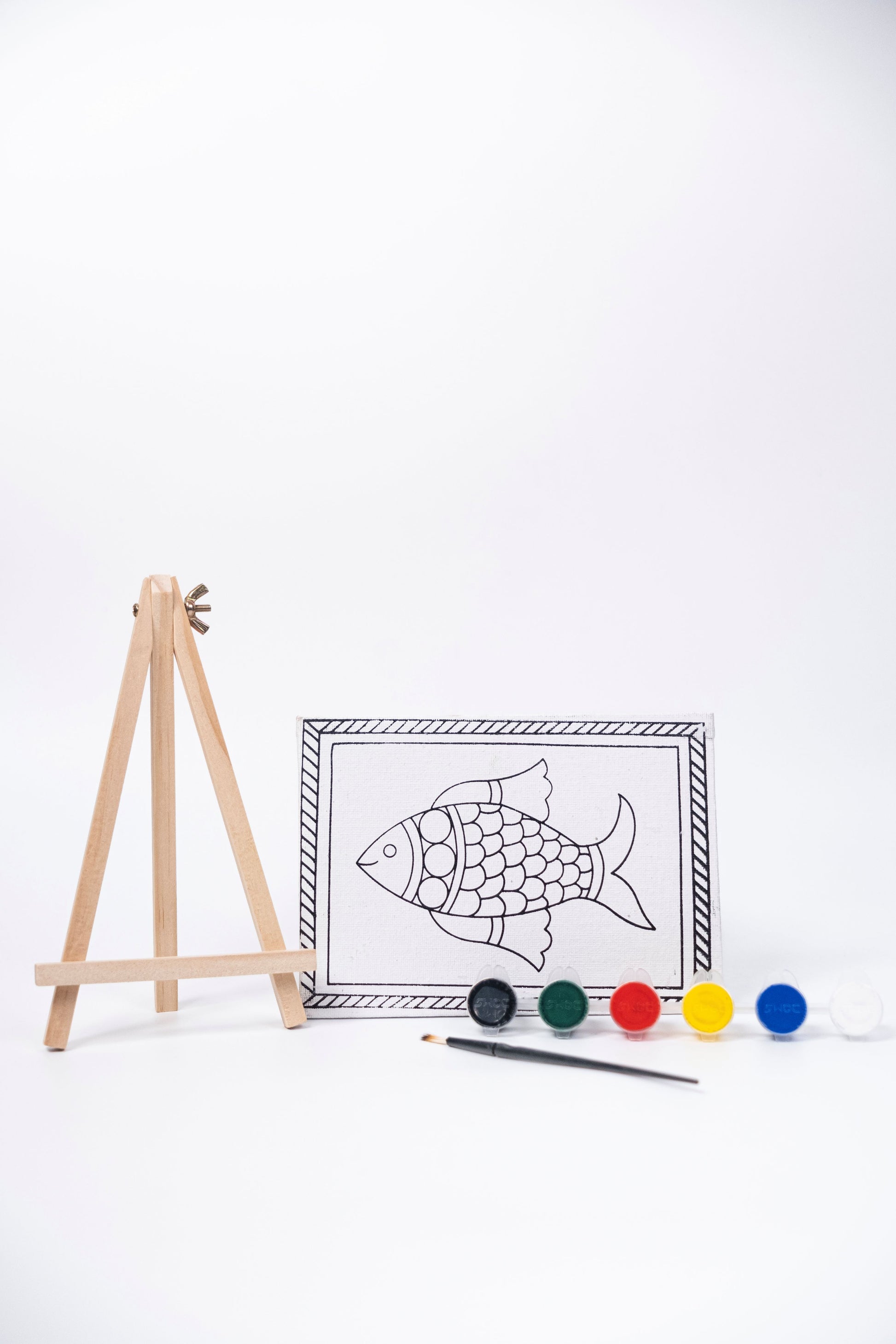 Contents of The Talking Canvas Madhubani Fish Canvas Wall Art DIY Kit with outlined fish canvas, wooden easel, brush and 6 acrylic paint pots.
