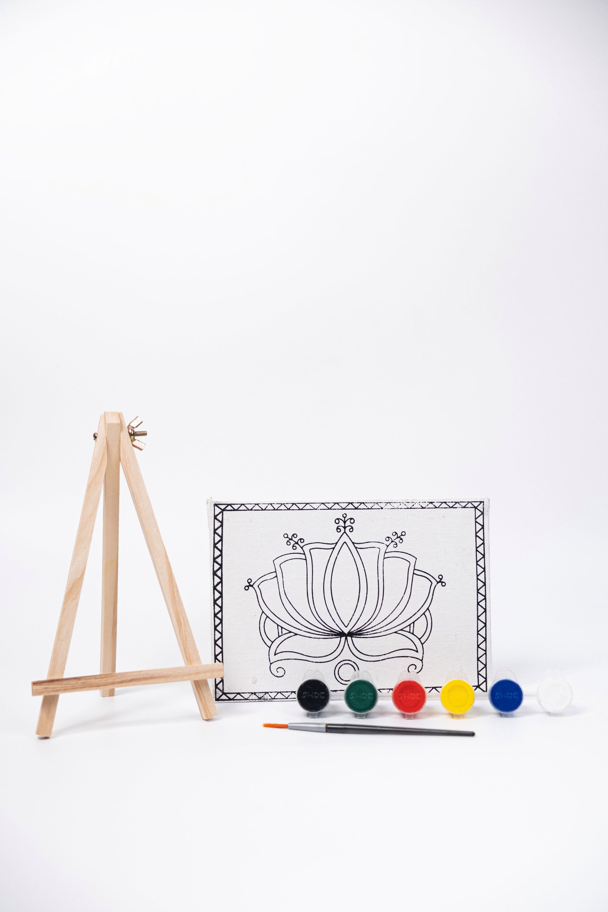 Contents of The Talking Canvas Madhubani Lotus Canvas Wall Art DIY Kit with outlined lotus canvas, wooden easel, brush and 6 acrylic paint pots.
