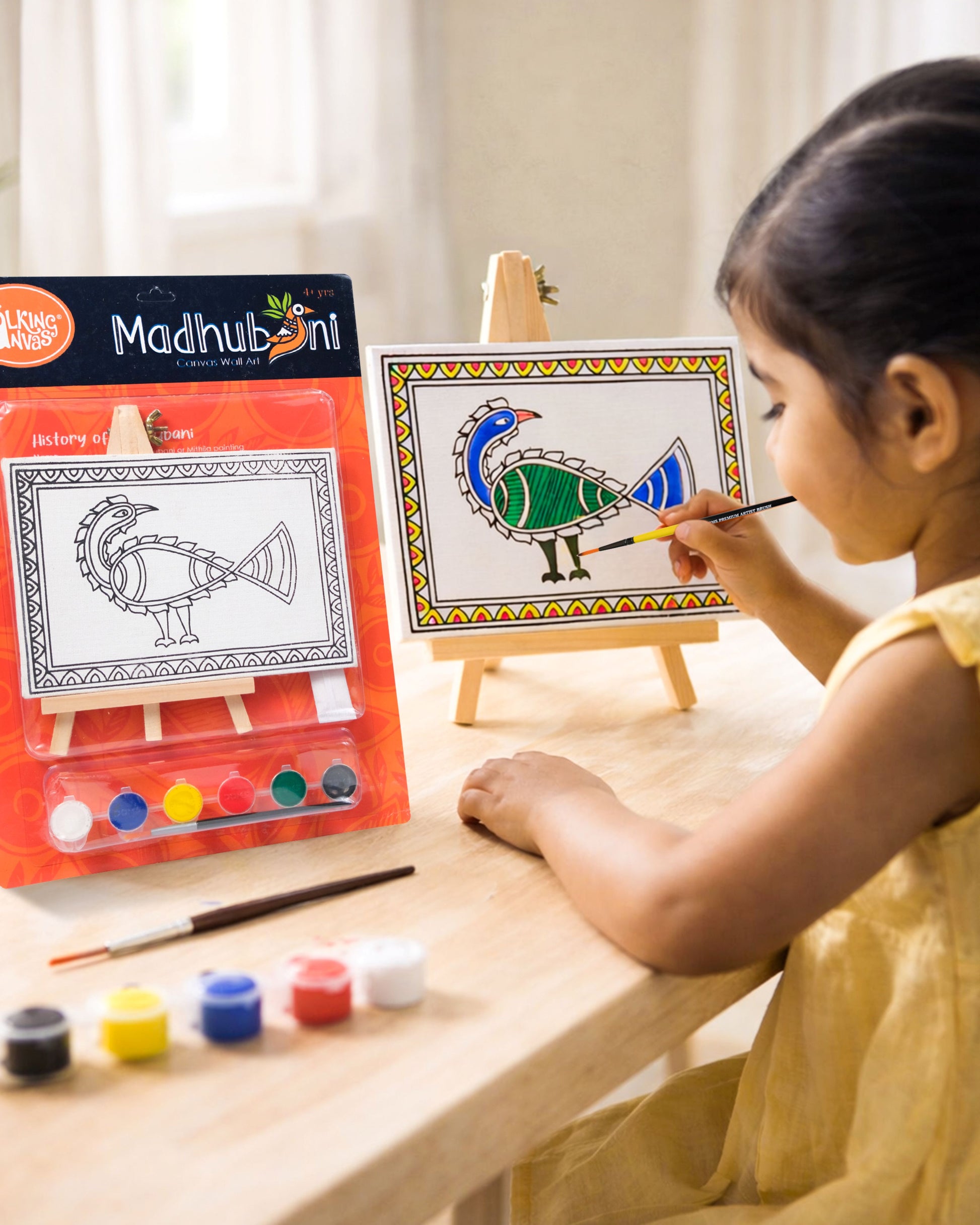 Child painting The Talking Canvas Madhubani Peacock Canvas Wall Art DIY Kit on a wooden easel using the included brush and acrylic paints.