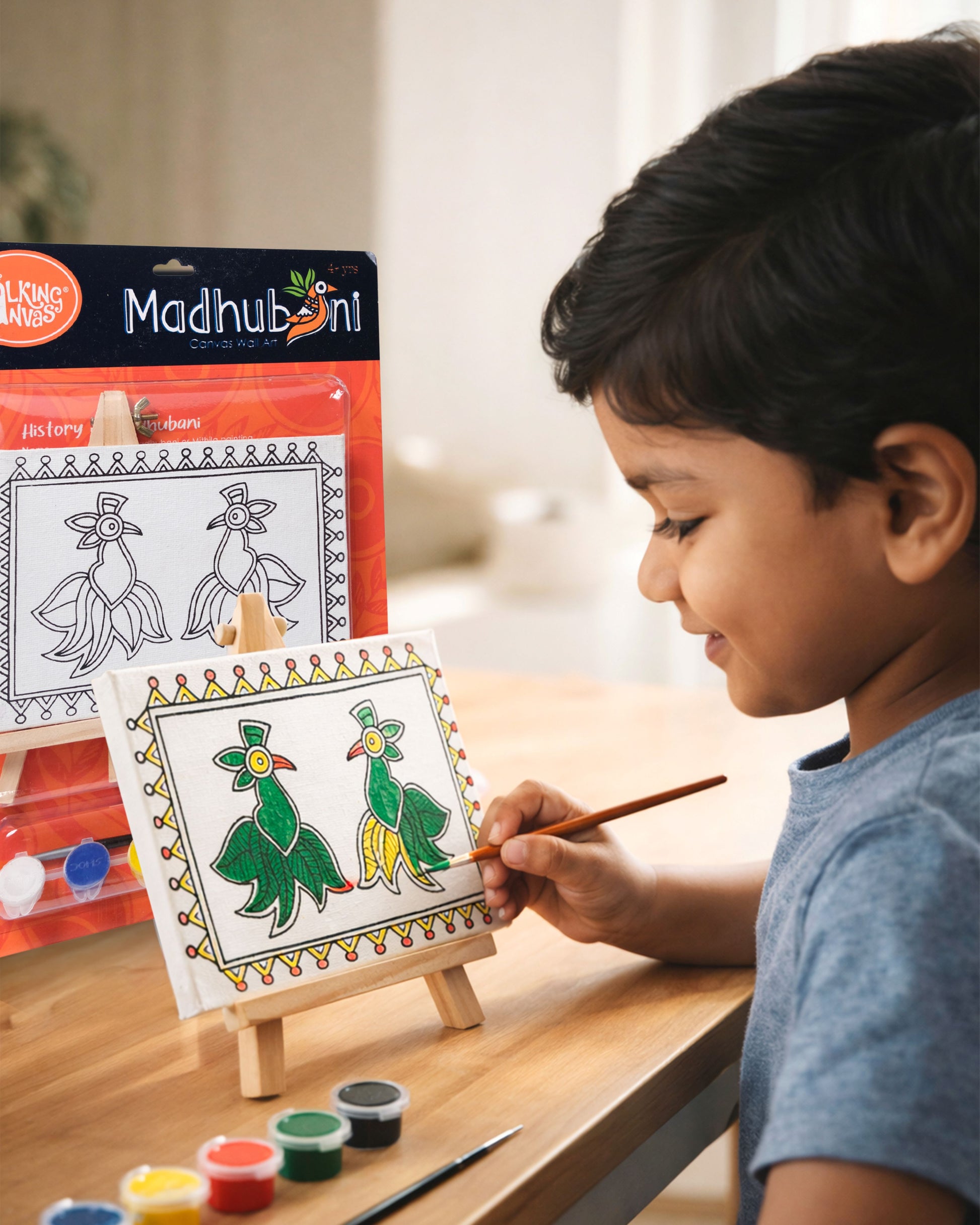 Child painting The Talking Canvas Madhubani Parrot Canvas Wall Art DIY Kit on easel using the included brush and acrylic paints.