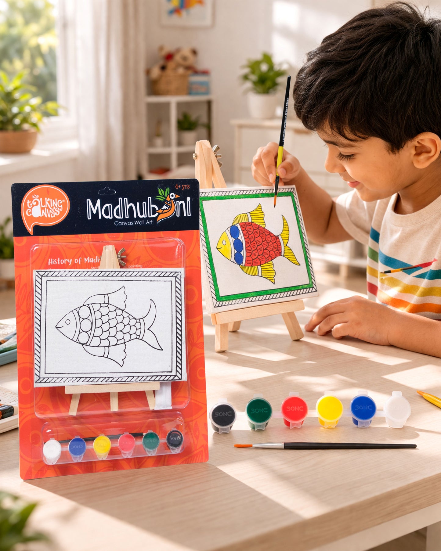 Child painting The Talking Canvas Madhubani Fish Canvas Wall Art DIY Kit on a wooden easel using the included brush and acrylic paints.