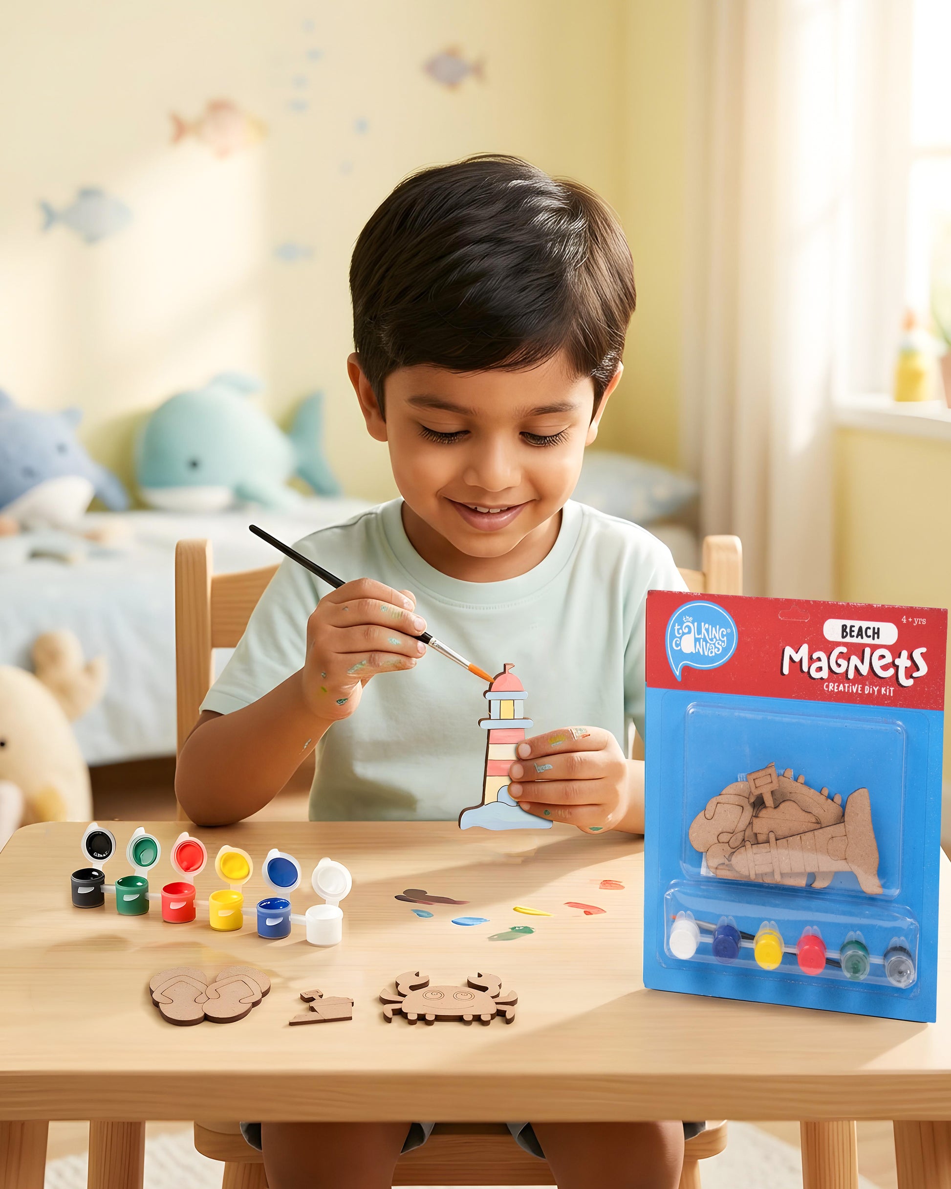 Child painting the lighthouse from the Beach Magnets Creative DIY Kit with wooden beach-themed magnets, acrylic paints and brush on a craft table.